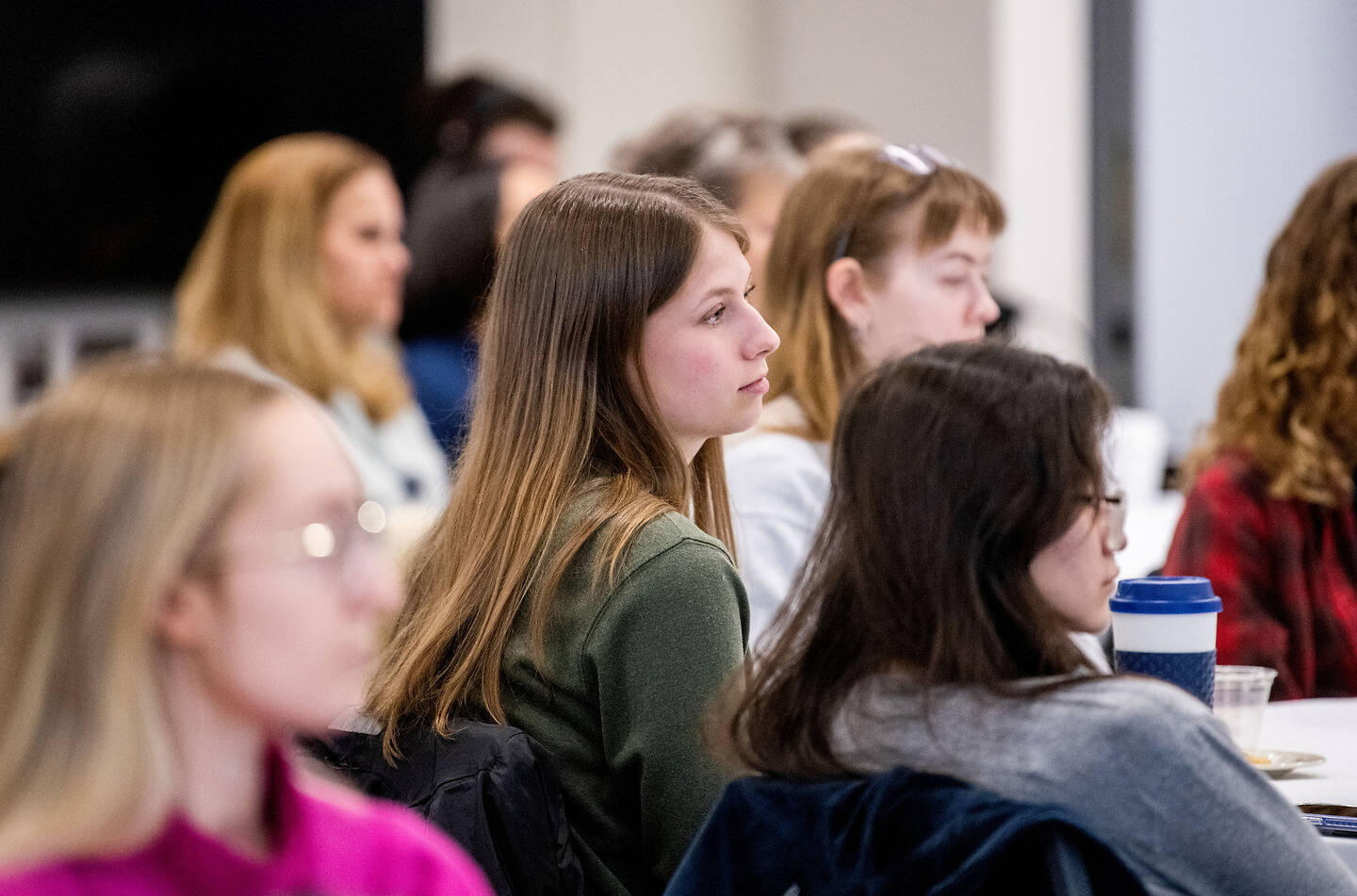 A group of young people sit attentively in a classroom, focused on something off-camera.